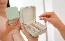 Young woman taking earring from jewelry box near mirror